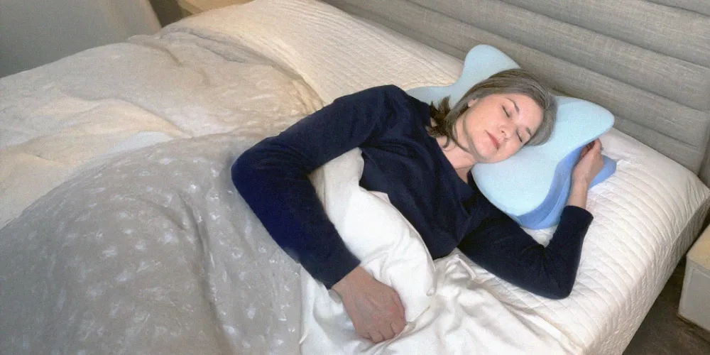 The Derila ERGO pillow in use on a made bed, with a side sleeper's head resting in the central hollow